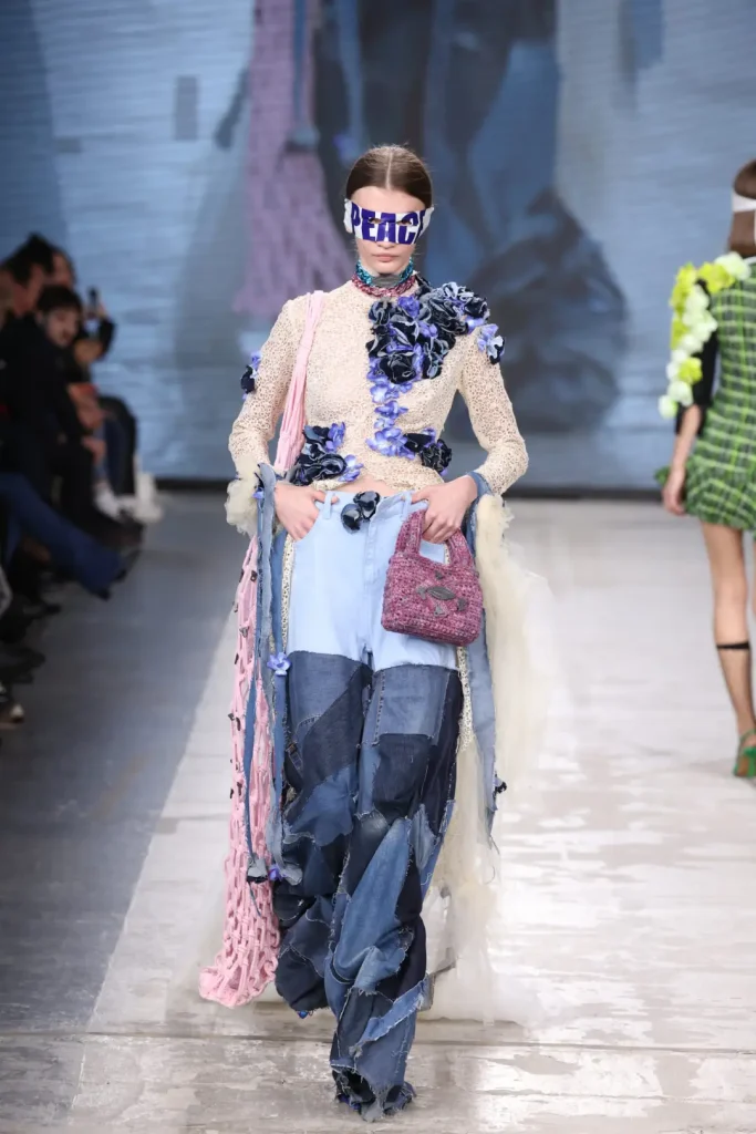 modella che sfila in fashion graduate con indosso un pantalone di denim, una borsa e un top