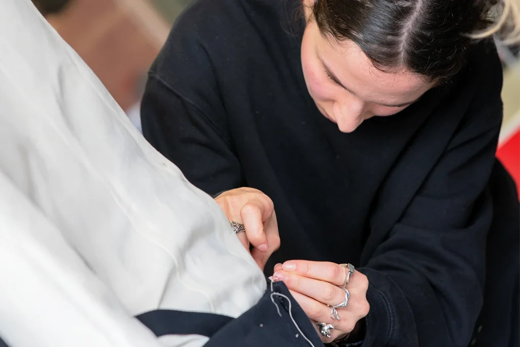 Studentessa cuce le finiture di un pantalone blu.