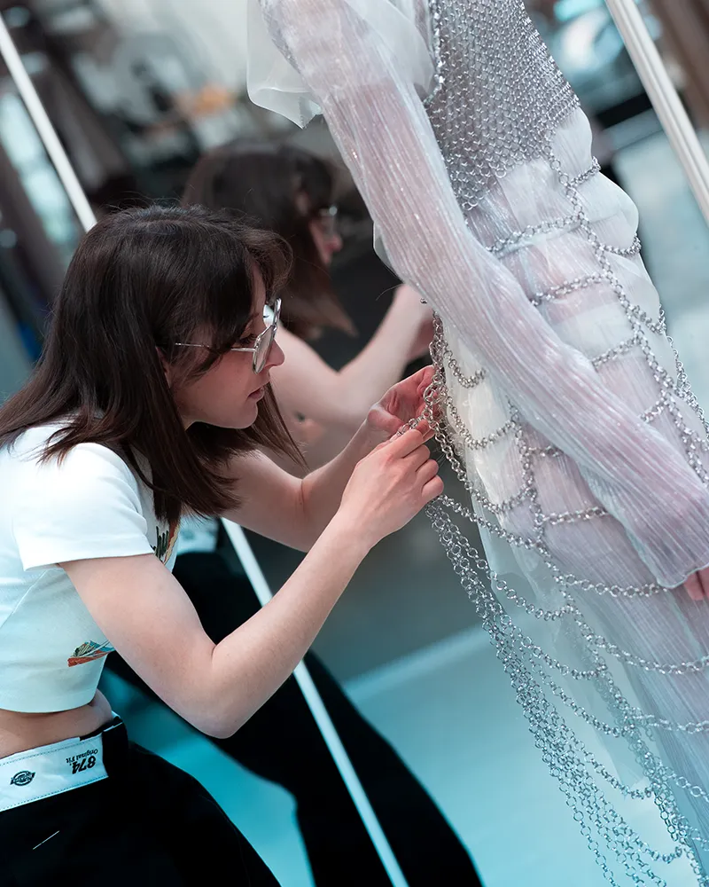 Studentessa lavora su un capo di maglia su una modella con un vestito bianco.