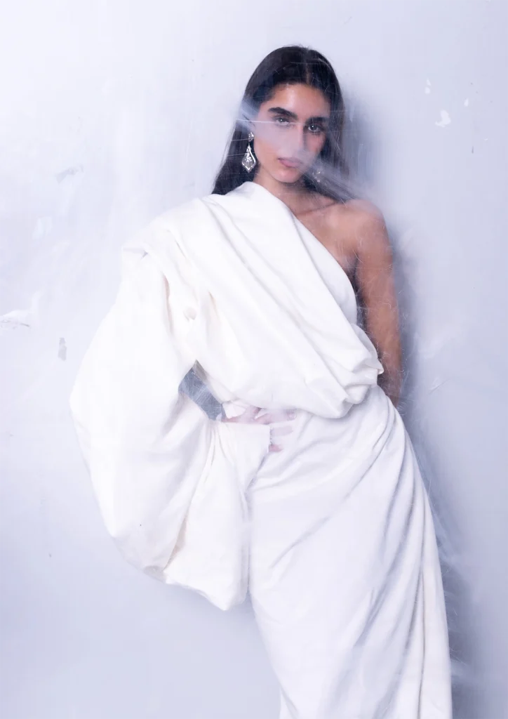 Modella in posa indossa un abito bianco con drappeggio sulla spalla.